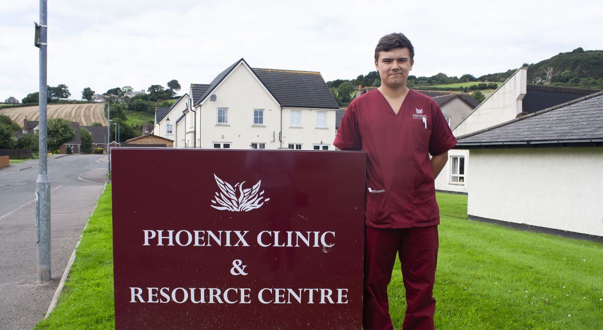 Corey Machala - a young man, wearing a burgundy healthcare uniform, pictured outside beside  Phoenix Clinic signage